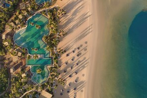 Luchtbeeld van een resort met meerdere zwembaden, een zandstrand en ligbedden.