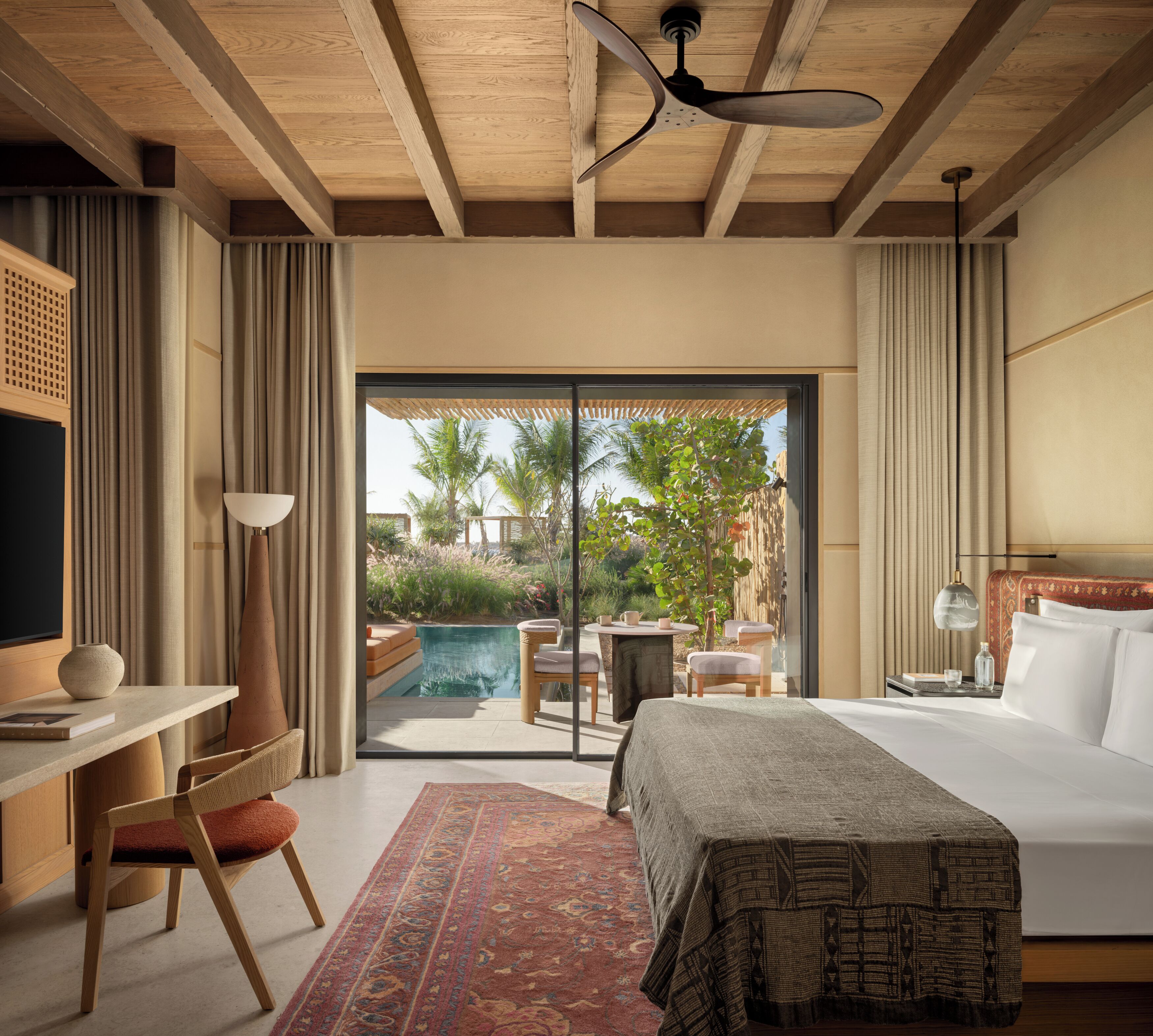 Quarto de hotel com cama, escrivaninha, cadeira e vista para uma piscina.