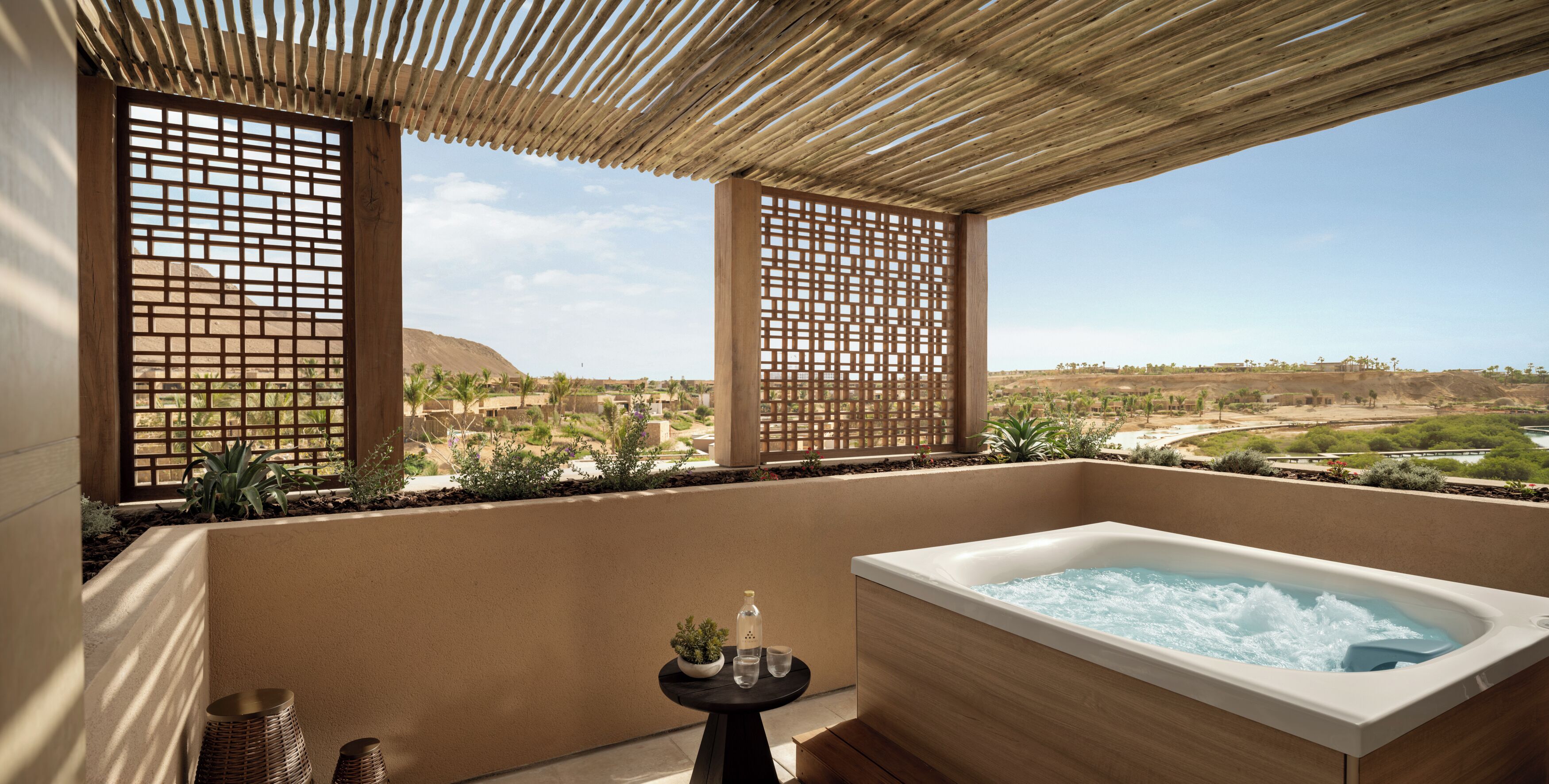 Un balcón con hidromasaje, ventanas con celosía de madera y vistas a un paisaje desértico.