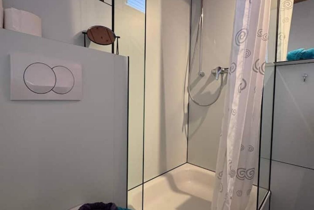 Une salle de bain moderne avec une douche à l’italienne en verre, une baignoire blanche et un porte-serviettes.