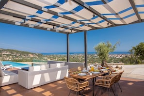 An outdoor dining area with a view of the sea and hills, a pool, and a covered seating area. - Villa Karyatis, Divine Sea & City Views, Infinity Pool, Furnished Terrace,. (Lefkada)