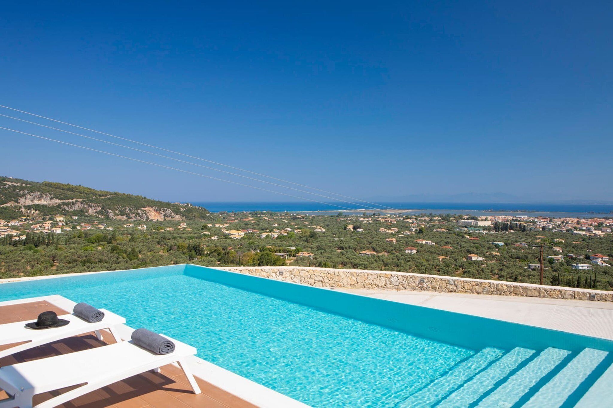 A clear blue sky, a swimming pool with lounge chairs, and a view of a coastal town.