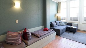 A modern living room with a sectional sofa, a small round table, and a lamp. - Apartment no. 01 (Warnemünde)