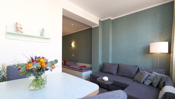A modern living room with a grey sofa, a small round table, and a vase of flowers on a white table. - Apartment no. 01 (Warnemünde)