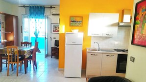A compact kitchen with a refrigerator, sink, and stove. There is a dining area with a table and chairs, and a black leather chair in the foreground. - Vacation Home in Otranto with 1 bedrooms sleeps 4 (Otranto)