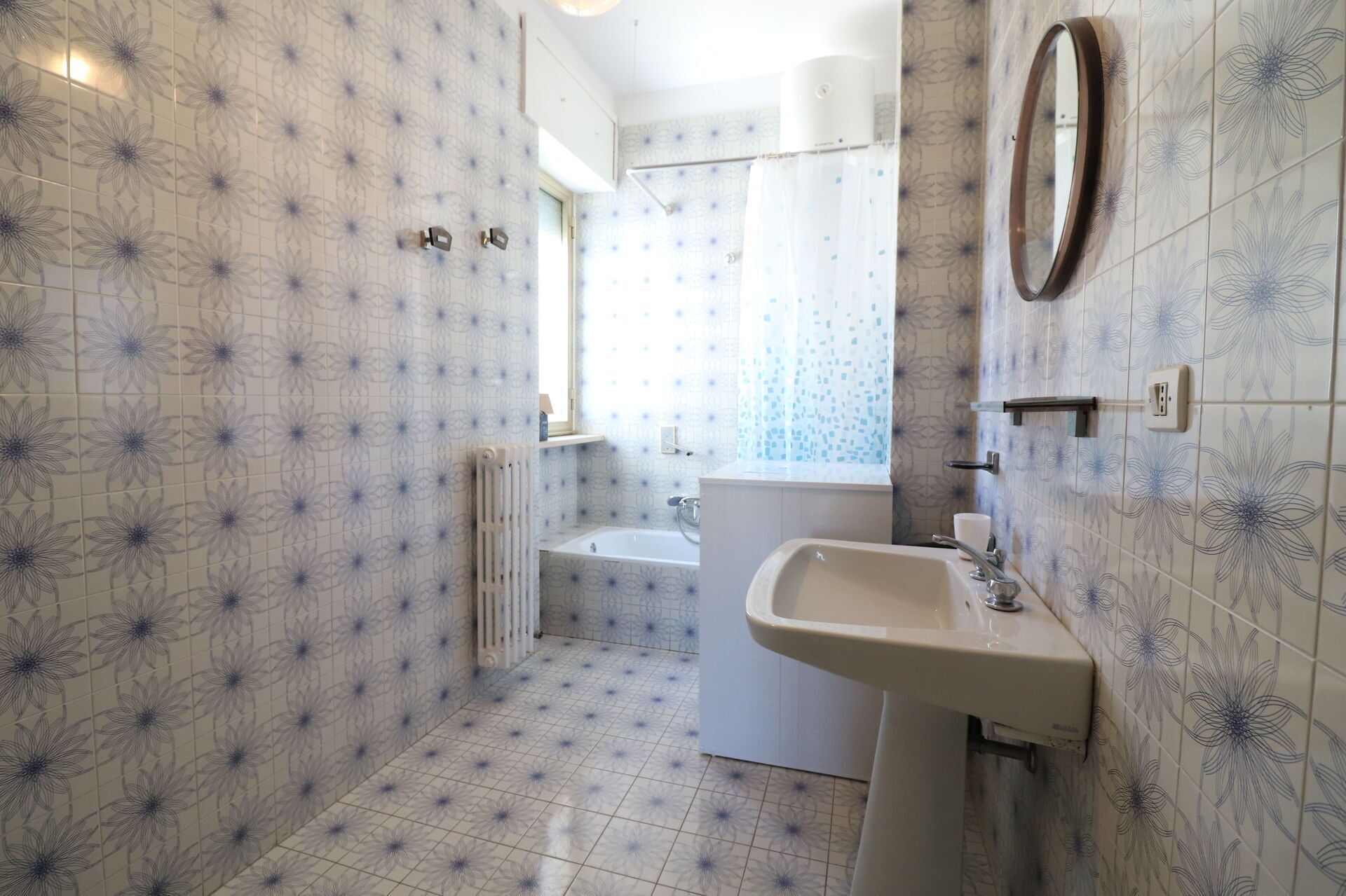 Une salle de bain avec des carreaux décorés, un lavabo, un miroir et un espace douche.