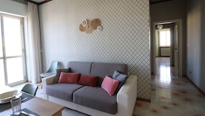 Un soggiorno con un divano grigio, carta da parati decorata e una zona pranzo con tavolo e sedie.