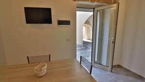 A dining area with a wooden table, two chairs, a television mounted on the wall, and a sliding glass door leading outside. - Vacation Home in Otranto with 2 bedrooms sleeps 4 (Otranto)