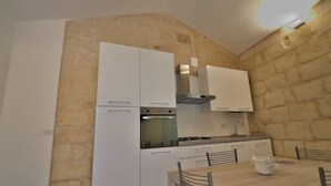 A compact kitchen with white cabinets, a stove, and a dining table with chairs. - Vacation Home in Otranto with 2 bedrooms sleeps 4 (Otranto)
