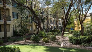 Un patio bien cuidado con un campo de mini golf, rodeado de árboles maduros y un edificio con balcones.