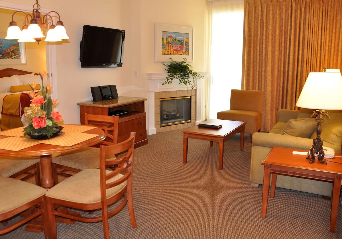 Una camera d'albergo con un tavolo da pranzo, sedie, un divano, una televisione, un camino e un quadro appeso al muro.