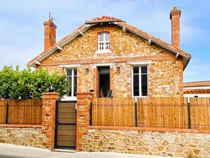 Ein Haus aus Stein mit Holzzaun, einem braunen Tor und zwei Schornsteinen.