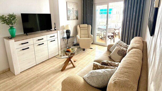 Una sala de estar moderna con un sofá, televisor y una mesa de centro de vidrio.