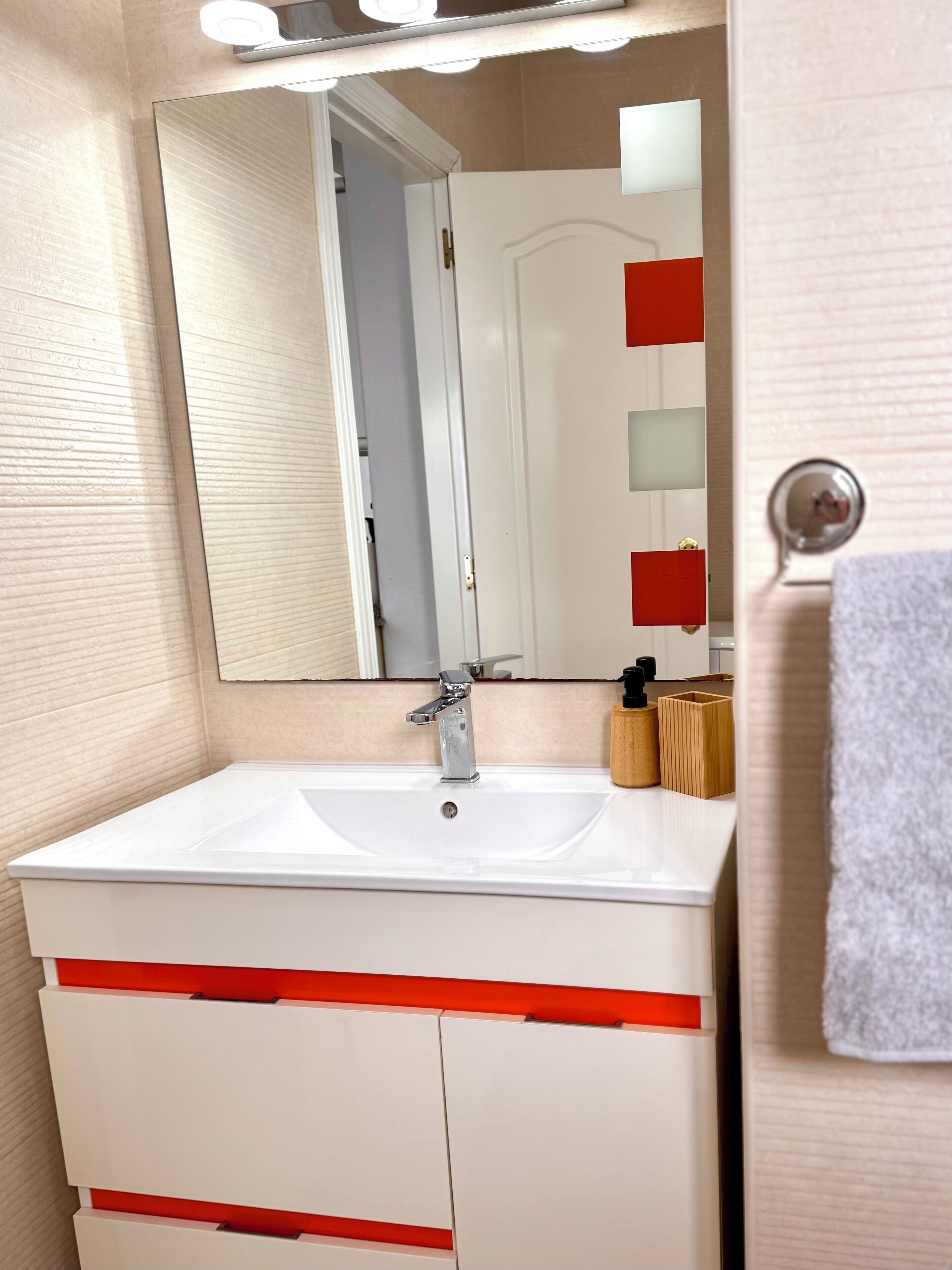 Een badkamer met een witte wastafel, rode accenten, een spiegel en een handdoekhouder.