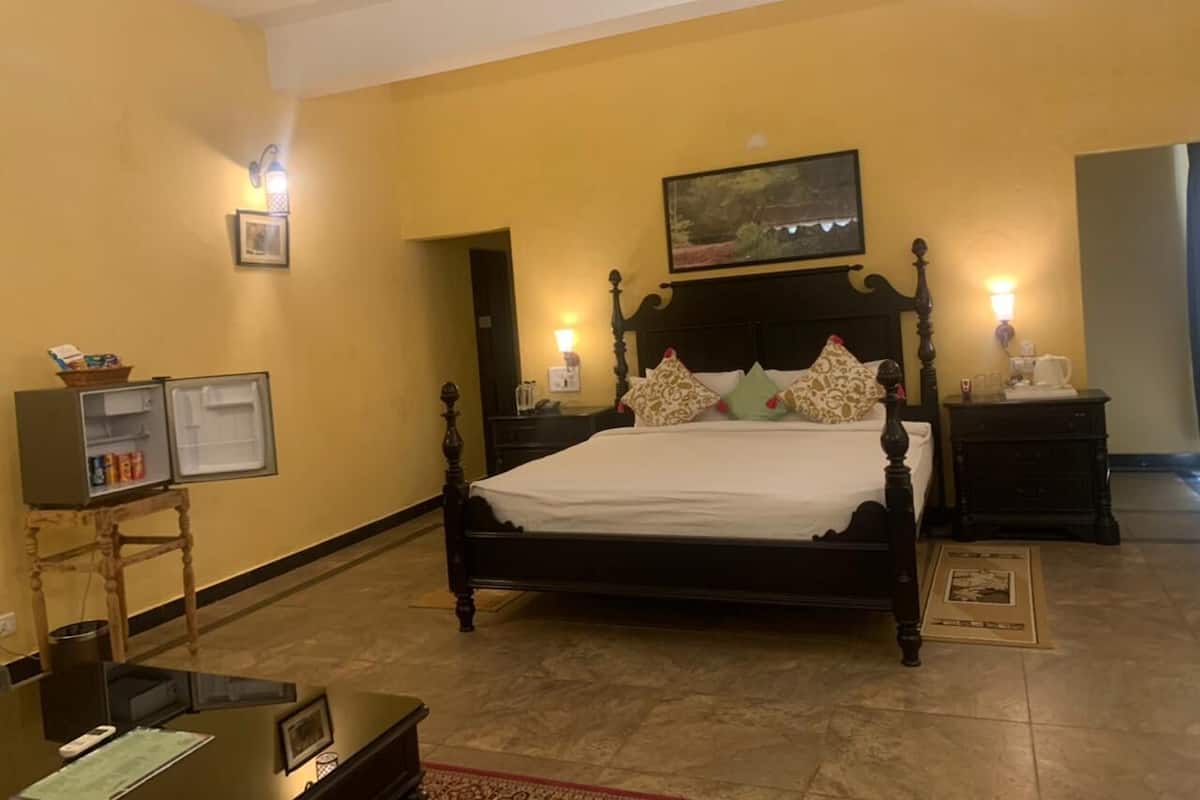 Un dormitorio con una cama grande, un ventilador de techo, un televisor sobre un mueble bajo y una pequeña mesa con una lámpara.