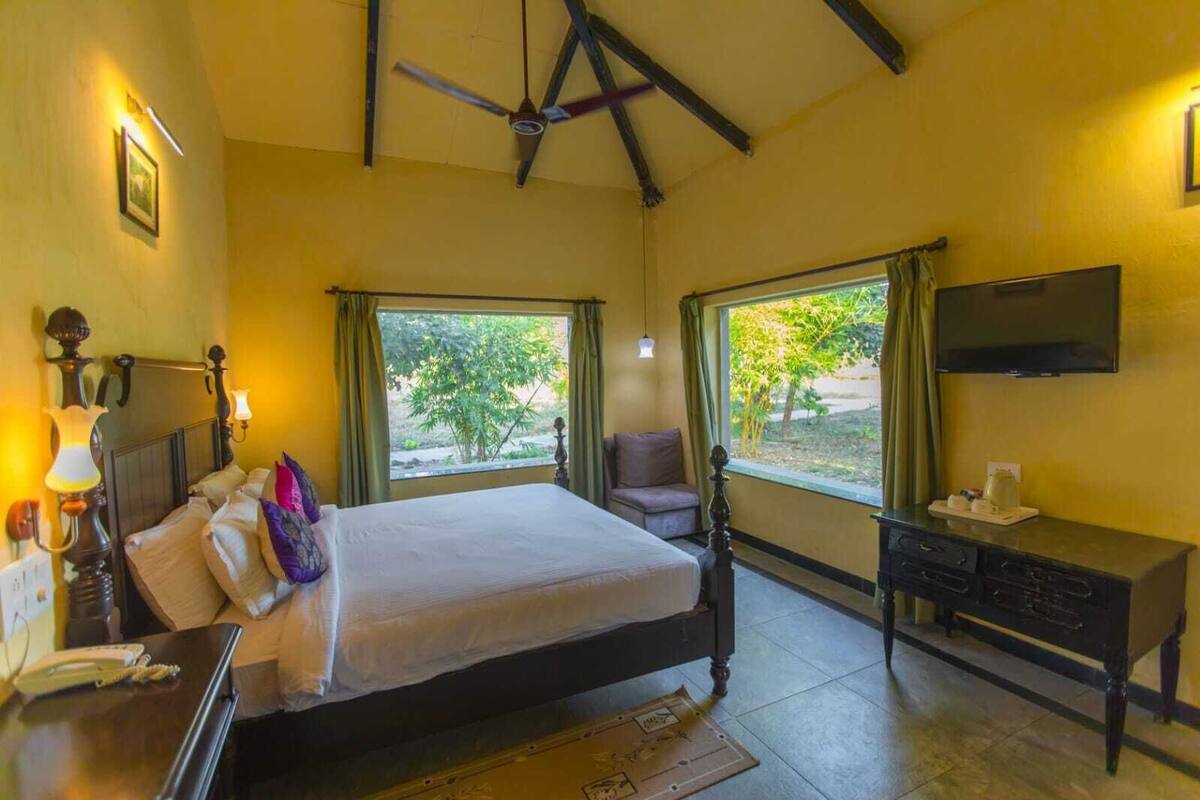 Un dormitorio con cama, escritorio, silla, televisor y ventanas amplias.