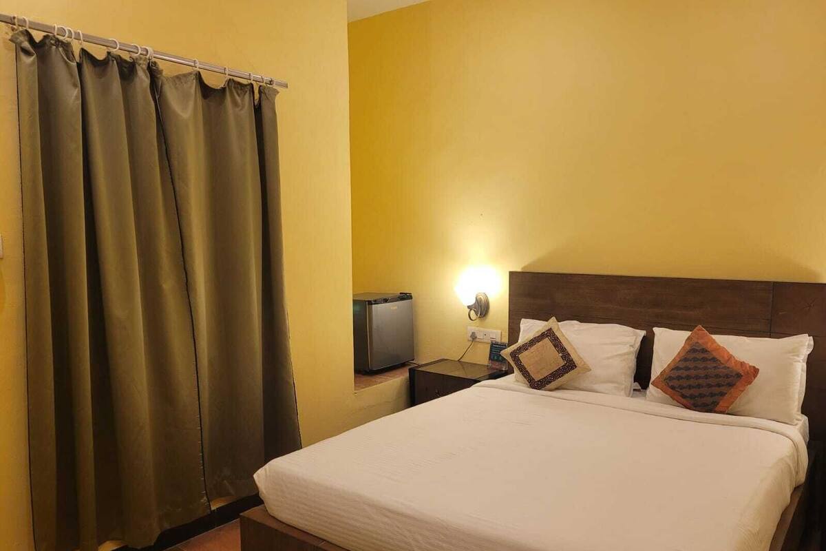 Una habitación de hotel con cama, cortinas, mesita de noche, televisión y una lámpara en la pared.