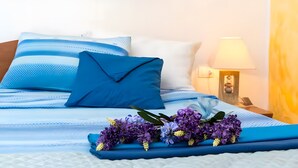 Een netjes opgemaakt bed met blauw-wit beddengoed, een blauw kussen en een bloemenarrangement op het bed.