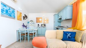 Een knus woongedeelte met een kitchenette, een eethoek en een bank met een kussen.