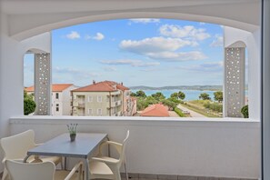 A balcony with a table and chairs, overlooking a coastal view with buildings and a road. - Sveti Filip i Jakov Apartment for 2 (Sveti Filip i Jakov)