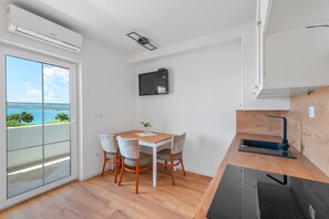 A small, modern kitchen with a dining area, a TV mounted on the wall, and a view of the sea through a large window. - Sveti Filip i Jakov Apartment for 2 (Sveti Filip i Jakov)