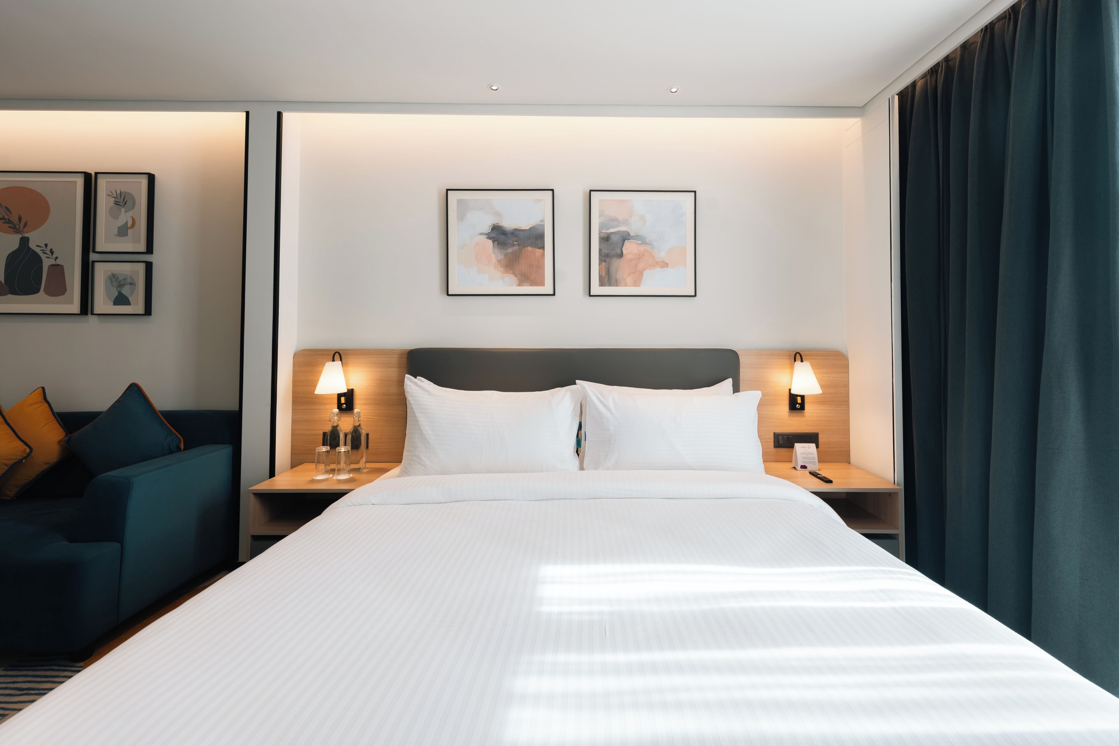 A hotel room with a large bed, two bedside tables with lamps, a sofa, and artwork on the walls.