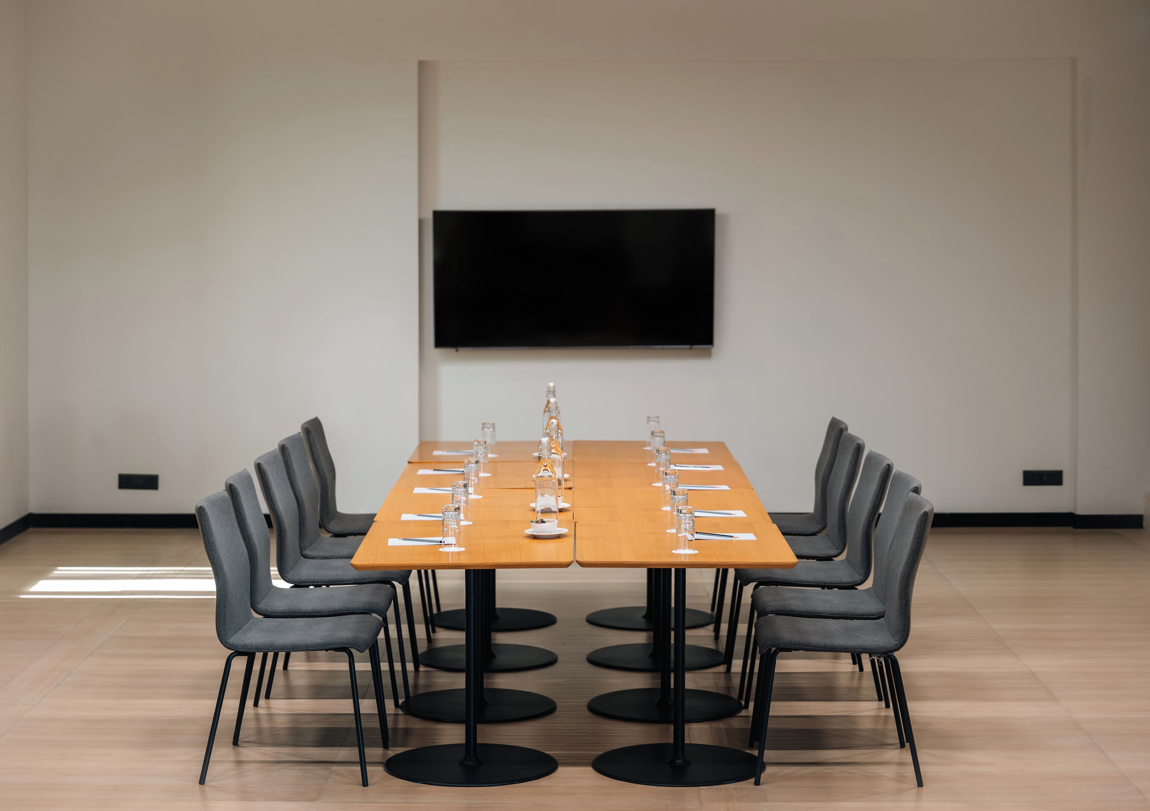 A conference room with a long table, chairs, and a flat-screen TV on the wall.