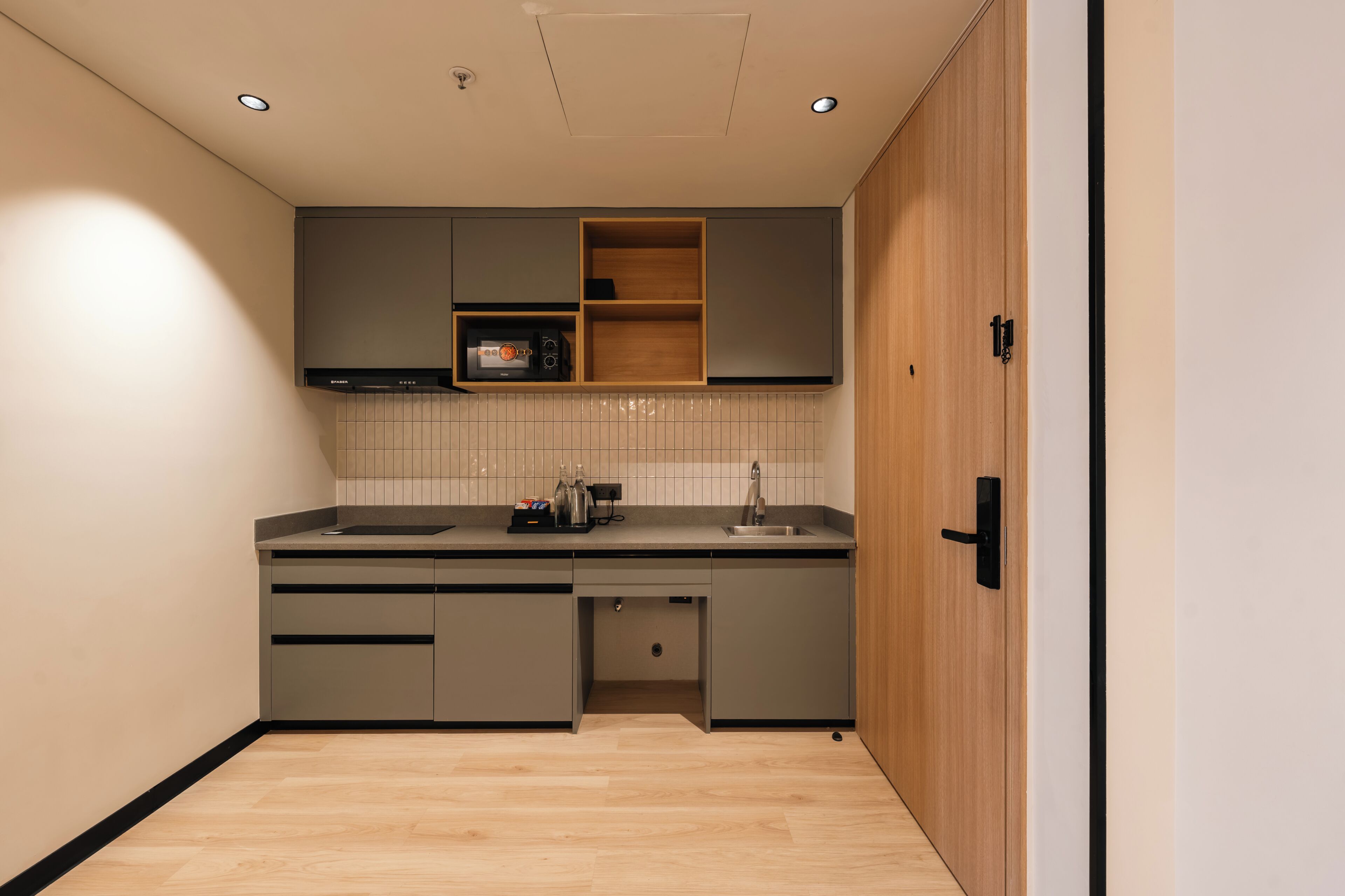Een moderne keuken met grijze kastjes, een houten deur en een betegelde spatwand.