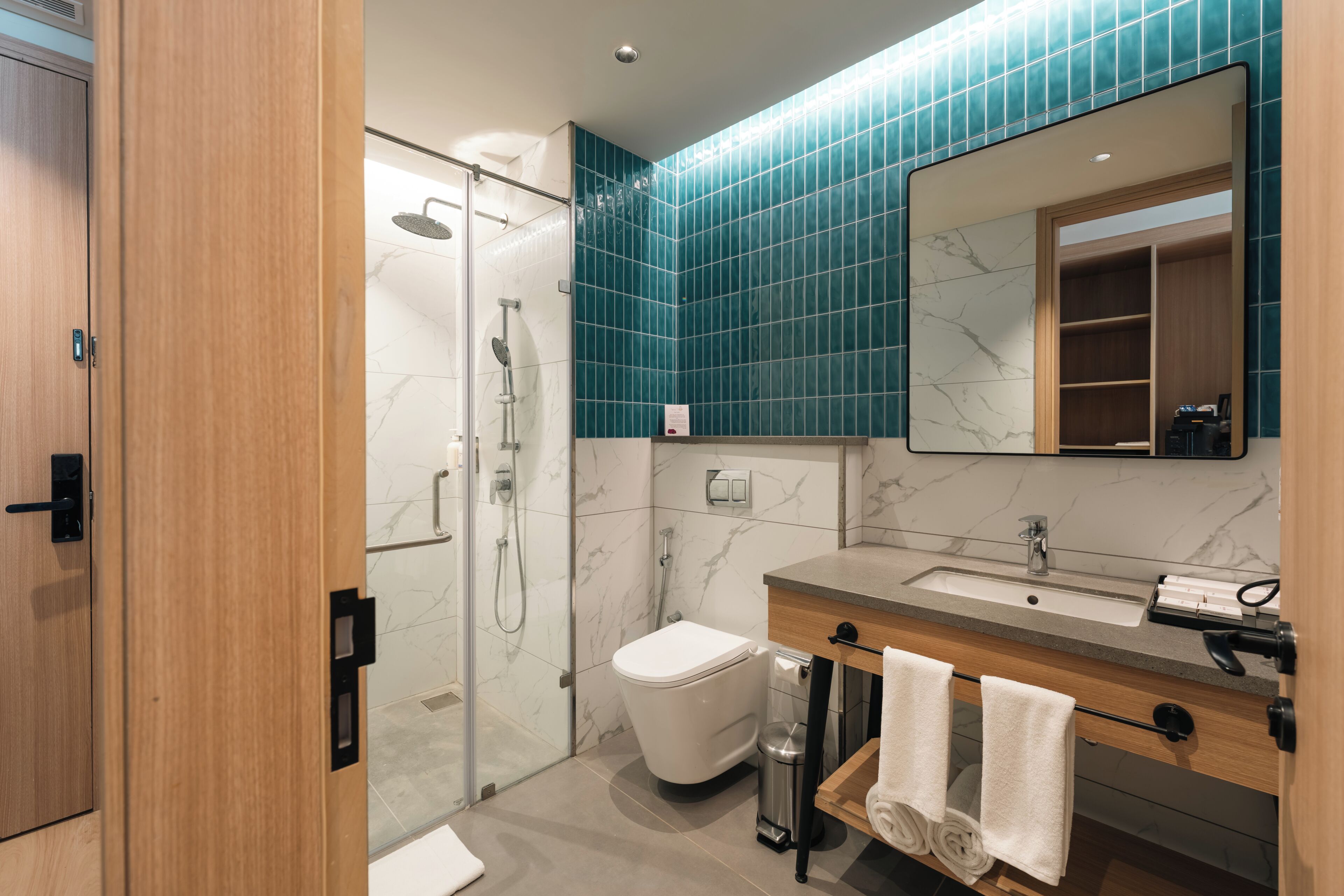 A modern bathroom with a glass shower enclosure, a white toilet, a sink with a marble countertop, and a mirror above the sink.