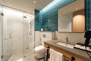Un bany modern amb un espai de dutxa de vidre, un vàter blanc, un lavabo amb mirall i una barra de tovalloles.