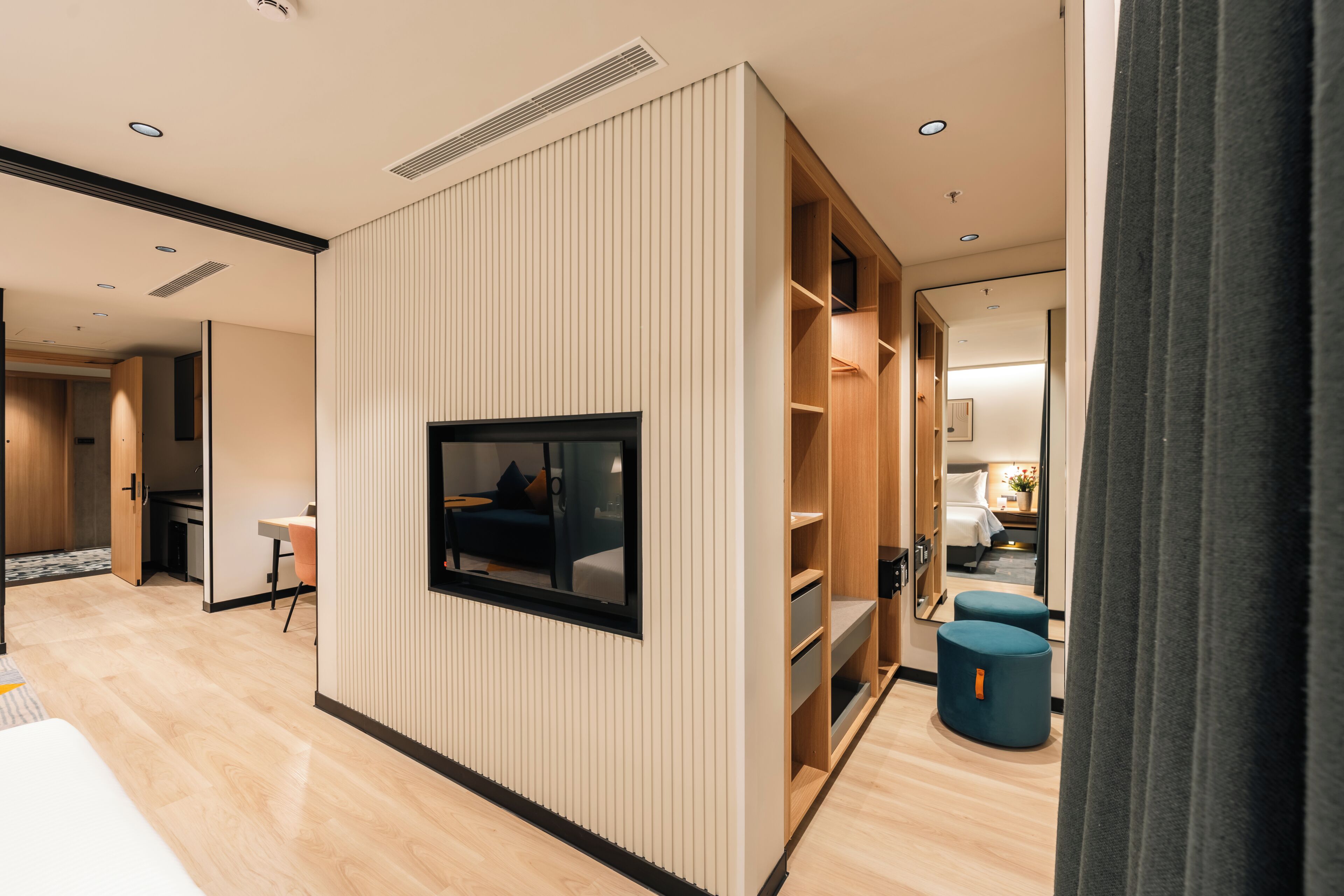A modern hotel room with a built-in TV, a wardrobe, a seating area, and a small table.
