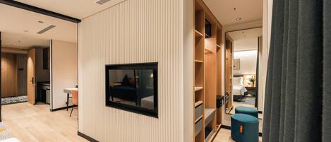 A modern hotel room with a built-in TV, a wardrobe, a seating area, and a small table.