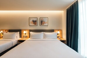 Habitació d'hotel amb dos llits, una taula de nit amb una làmpada, una obra d'art penjada a la paret i una finestra amb cortines.