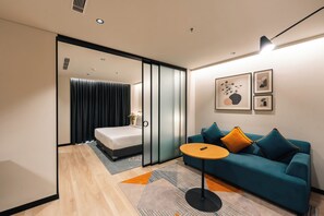 Habitació d'hotel moderna amb llit, sofà, taula petita i obra d'art a la paret.