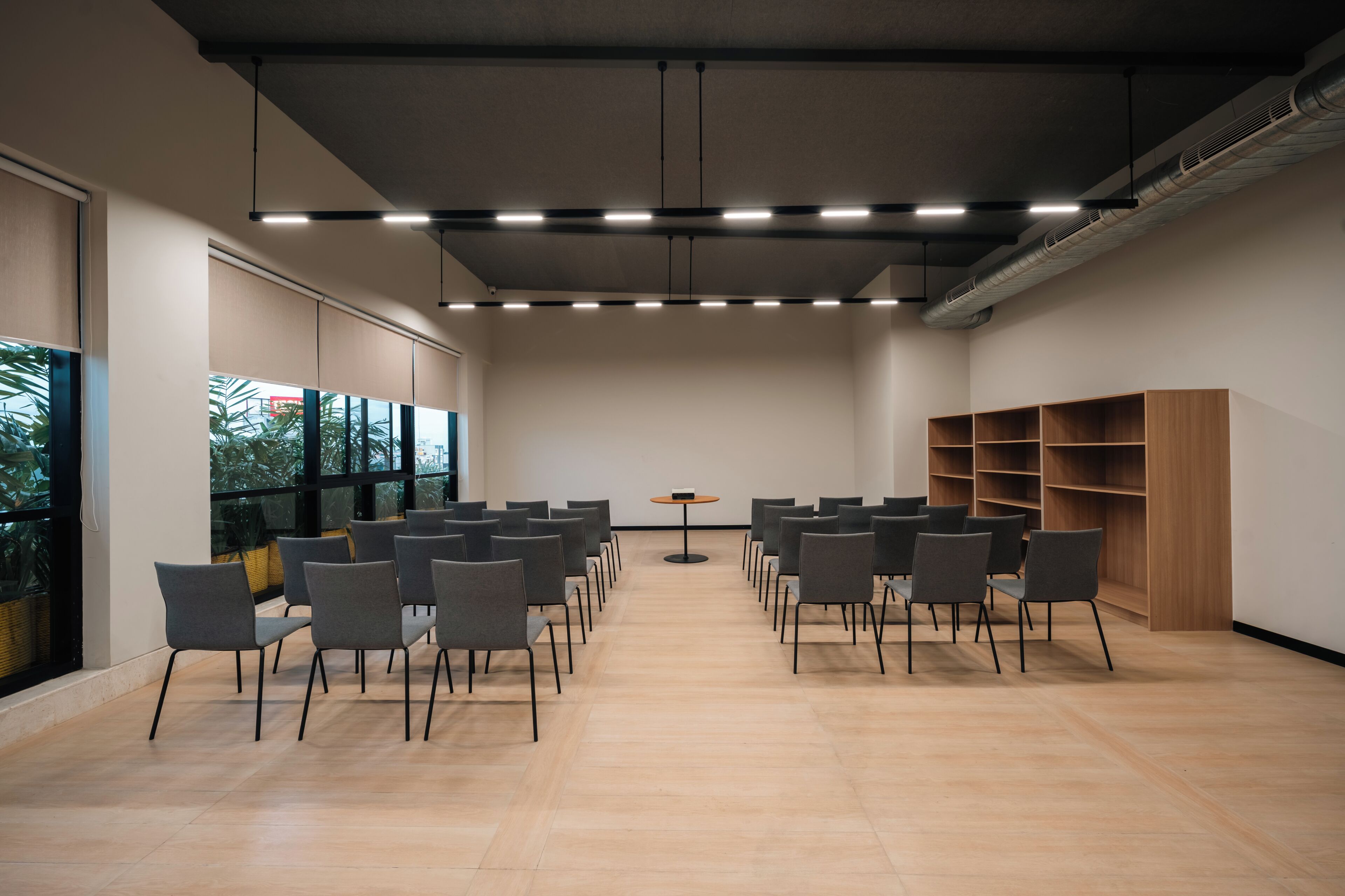 Una sala de conferències amb files de cadires, una taula central i una prestatgeria.