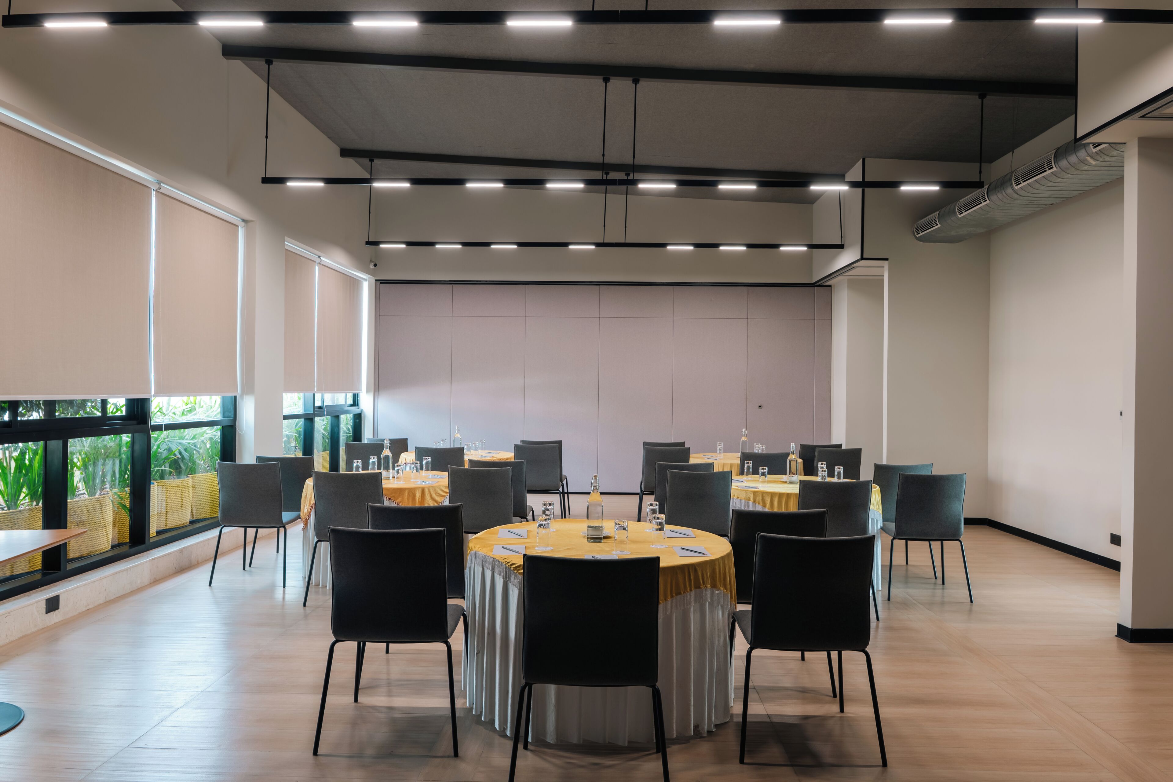 A conference room with round tables, black chairs, and a view of greenery through large windows.