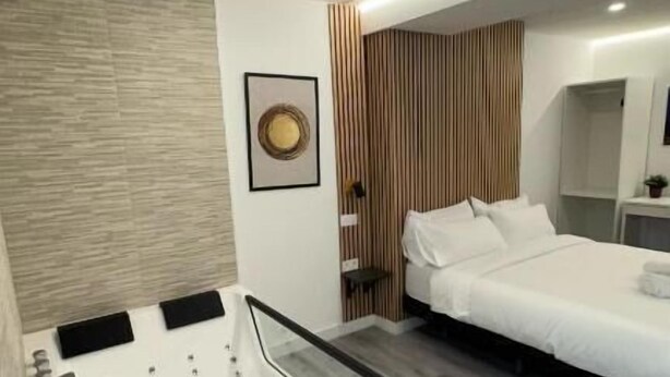 A modern bedroom with a large white bed, a built-in massage table, and a wooden floor. - jacuzzi rooms (Madrid)