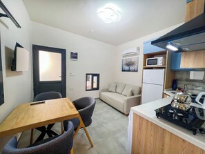 A compact living space with a kitchenette, a dining area with a wooden table and chairs, a sofa, and a small TV. - Paddys Pansiyon (Fethiye)