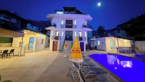 A hotel with a pool, outdoor seating, and a moonlit night sky. - Paddys Pansiyon (Fethiye)