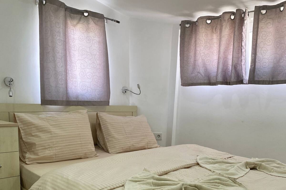 A neatly made bed with a striped bedspread, a bedside table, and a wall-mounted light fixture.