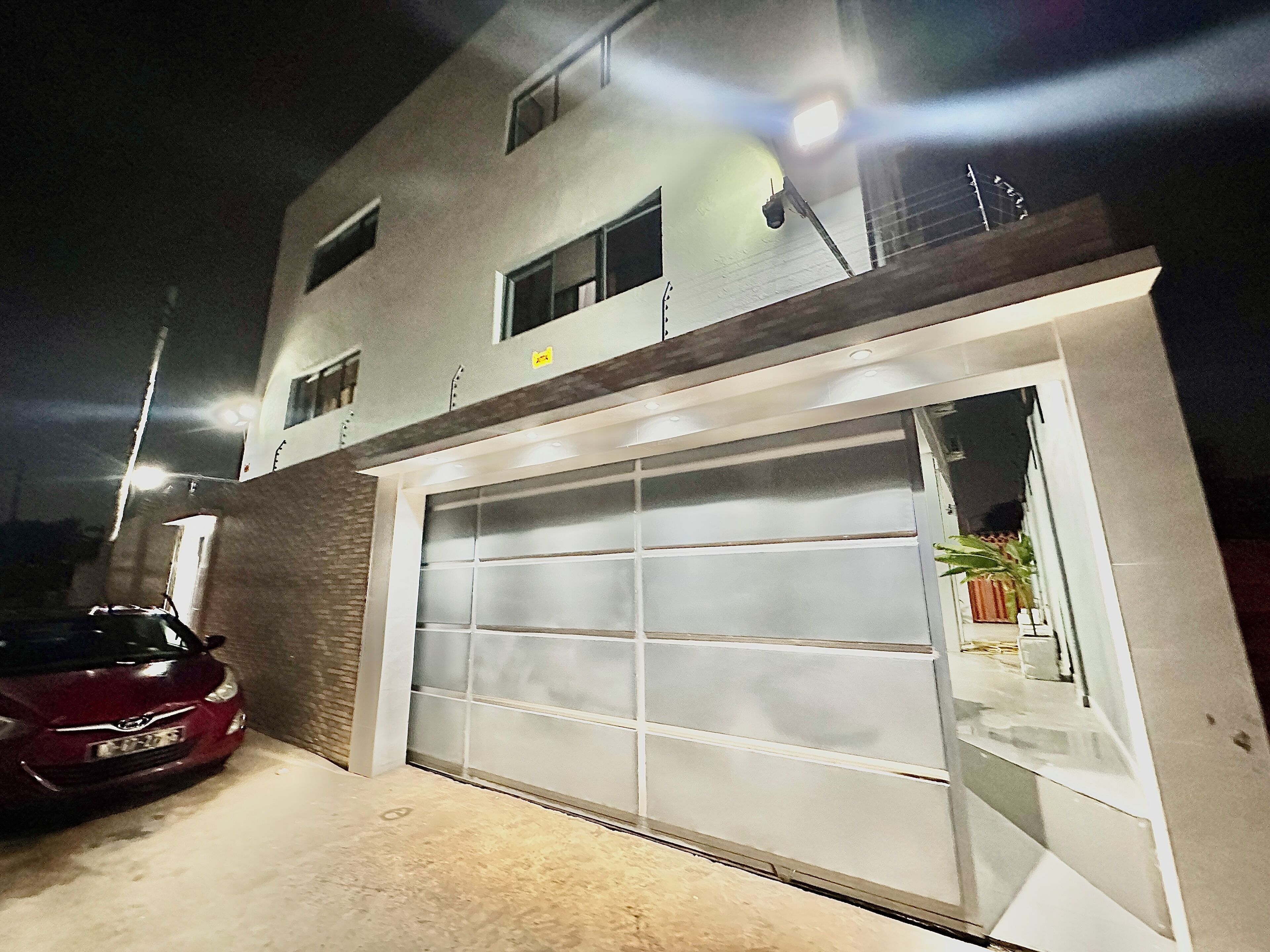 A modern building with a garage door, a parked car, and a potted plant near the entrance.
