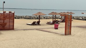 Een strand met houten ligbedden en parasols, een houten hek en een rotsachtige kustlijn.
