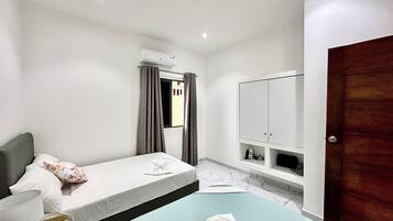 A bedroom with two beds, a wardrobe, a window with curtains, and an air conditioning unit.