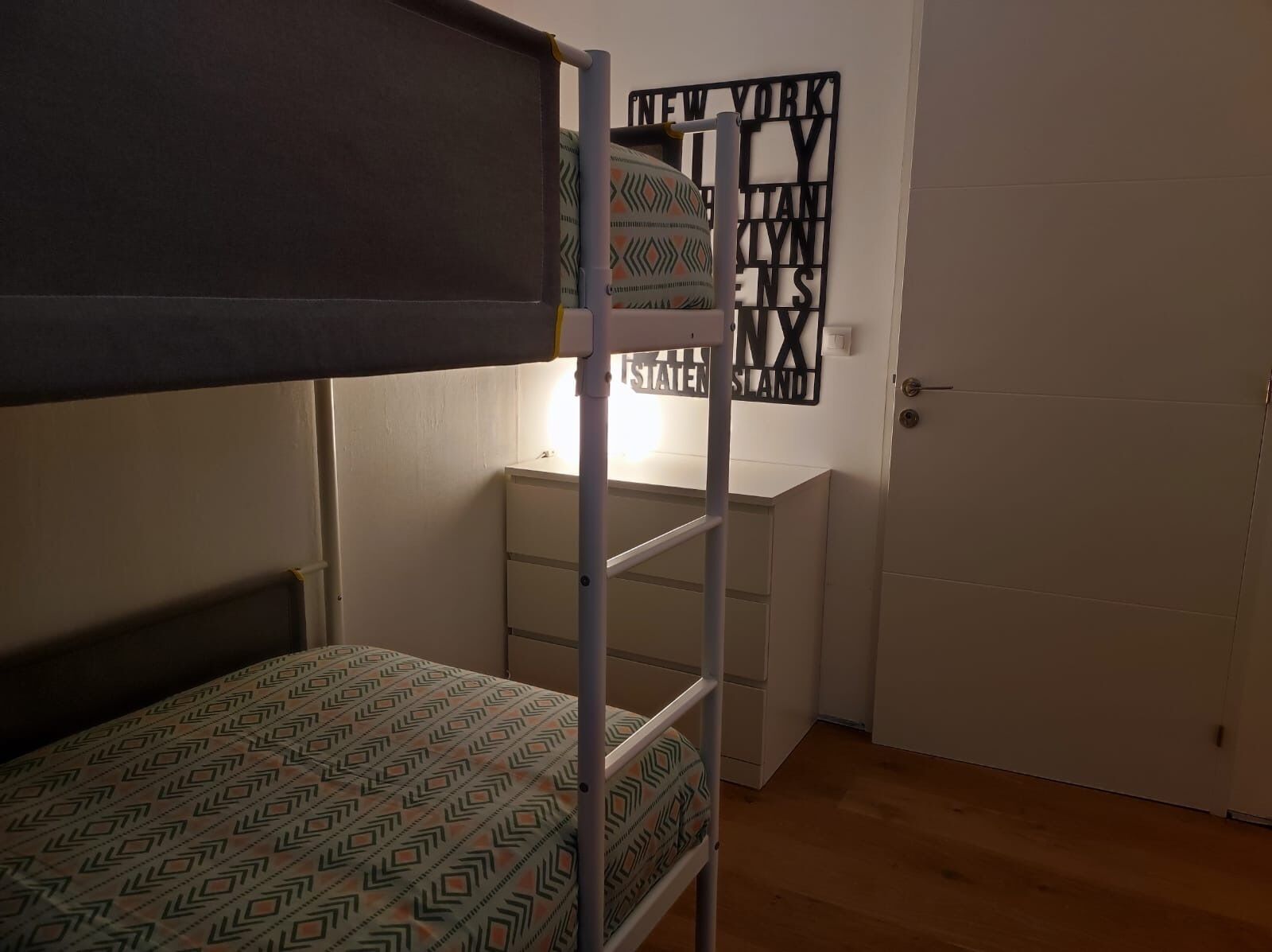 A bunk bed with patterned bedding, a desk with drawers, and a door with a decorative sign.