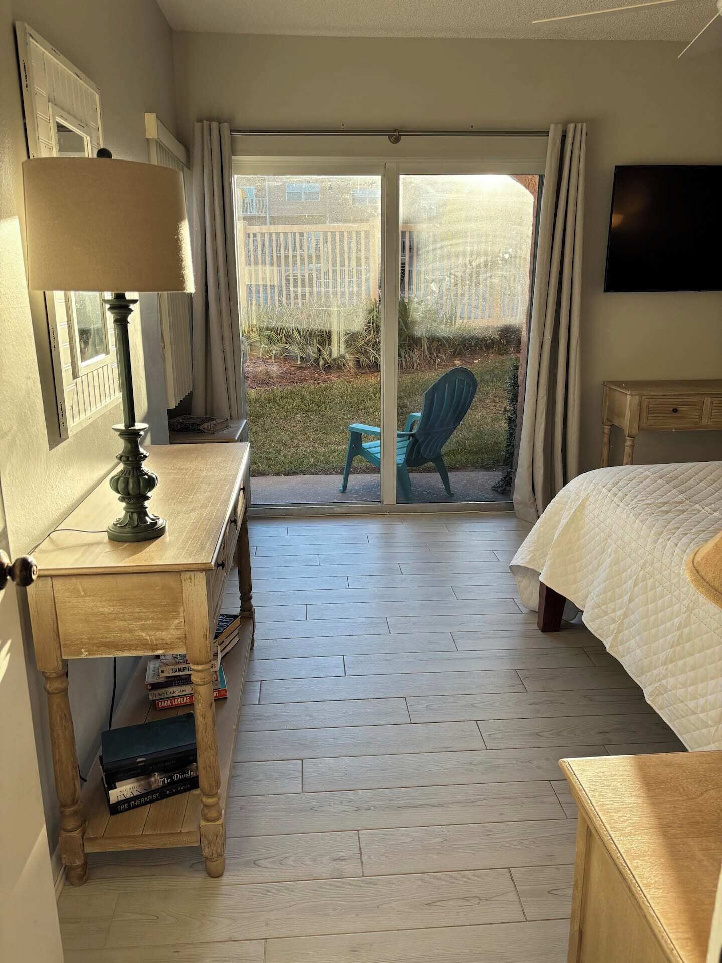 Une chambre d’hôtel avec un lit, un bureau doté d’une lampe, une chaise et un téléviseur. Une porte-fenêtre coulissante donne sur un balcon où se trouve une chaise.