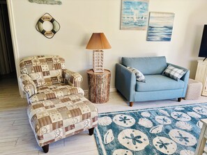Una sala de estar con un sillón estampado, un sofá azul, una mesita de madera con una lámpara y una alfombra decorativa.