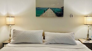Une chambre d’hôtel avec un lit, deux tables de chevet, deux lampes et un tableau représentant une jetée.