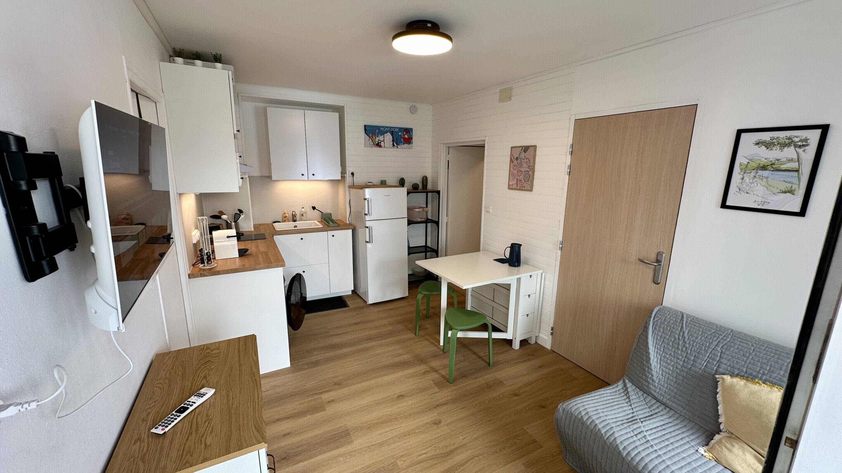 A compact kitchen with white cabinets, a refrigerator, and a small dining table with green chairs.