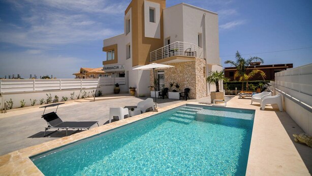 Et moderne hus med to etager, en swimmingpool, udendørs siddepladser og et apoteks skilt.