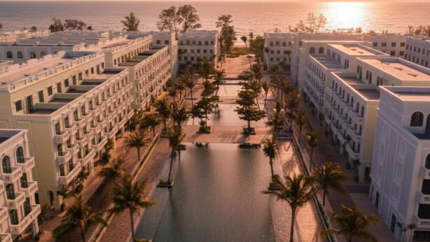 Un hôtel doté d’une piscine centrale, entouré de palmiers et de bâtiments avec des balcons.